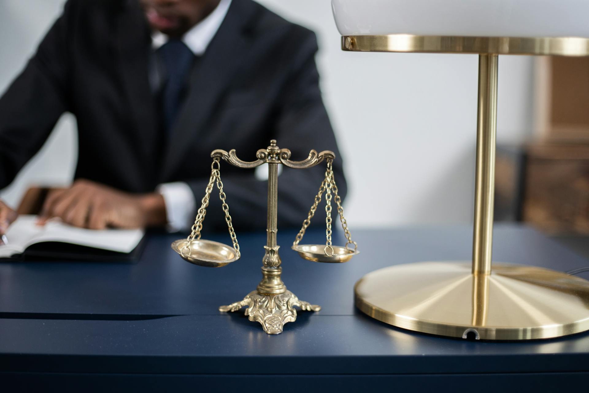A weighing scale, A table lamp, a man in a black suit with blue toe and white shirt writing on a paper